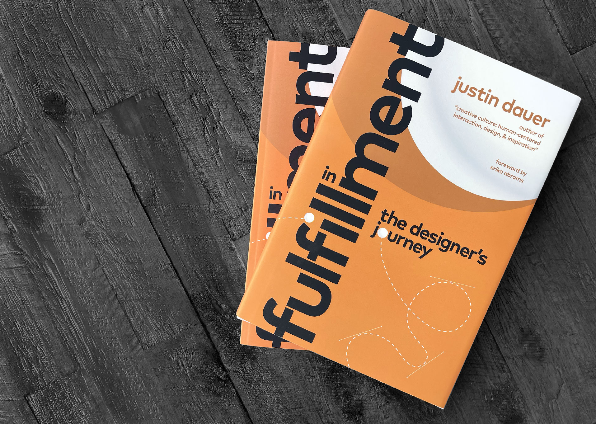 a couple copies of the hardcover book In Fulfillment: The Designer's Journey resting on a wood table